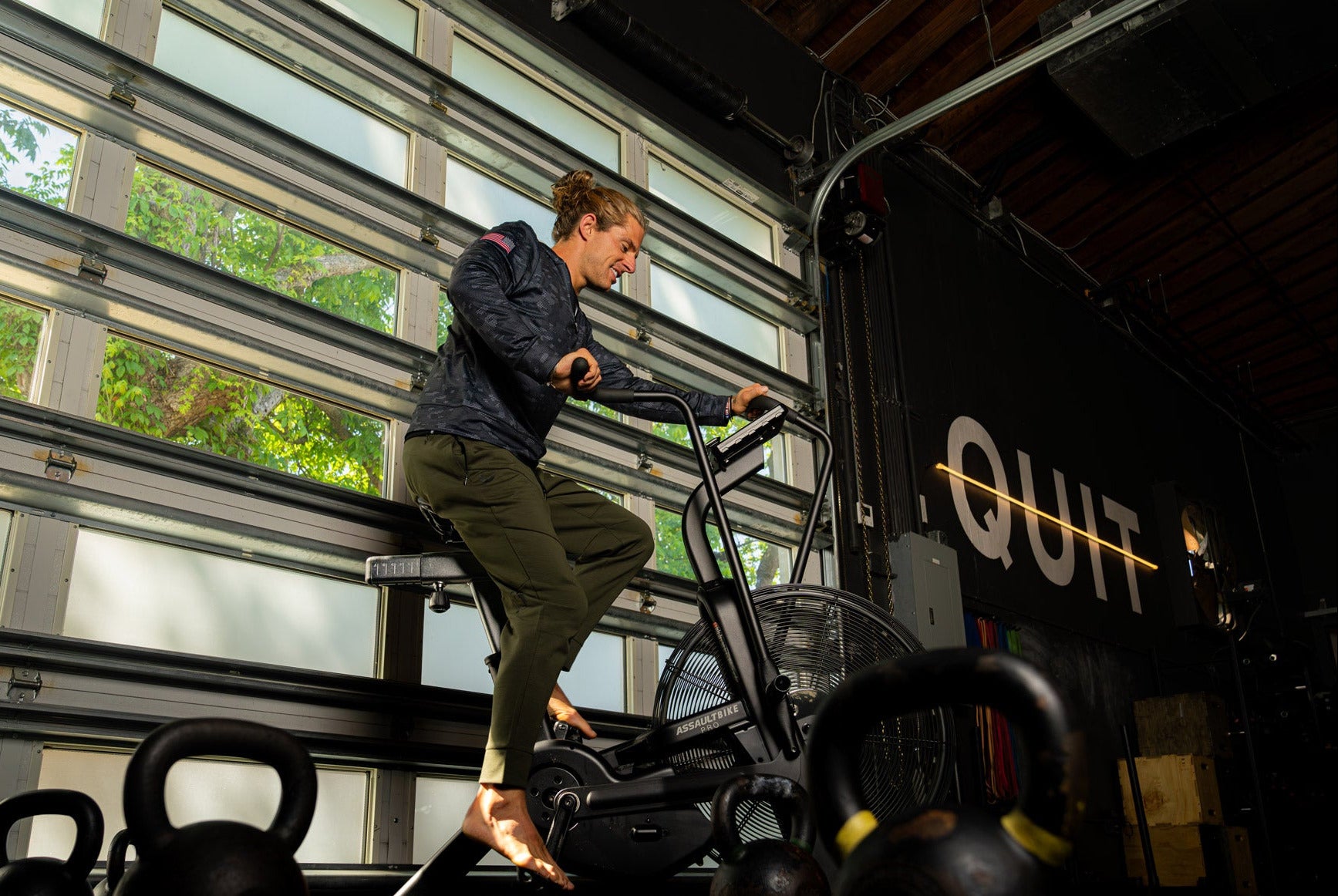 Person using a stationary bike in a gym setting with kettlebells in the foreground.